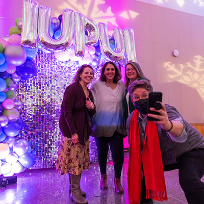 The campus community celebrates the holiday in style at the annual IUPUI Holiday Open House. People pose for selfies in front of a shiny decorative temporary wall. 