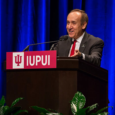 Chancellor Nasser Paydar standing at IUPUI podium with blue stage curtain behind him