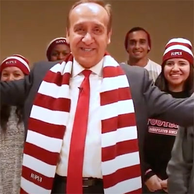 IUPUI Chancellor Nasser Paydar wearing red and white striped scarf and surrounded by IUPUI students who are wearing red and white striped stocking caps