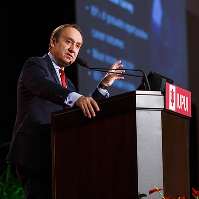 Chancellor Paydar standing at IUPUI-branded podium with a PowerPoint slide in the background.  The content of the slide is not clear because of the angle.