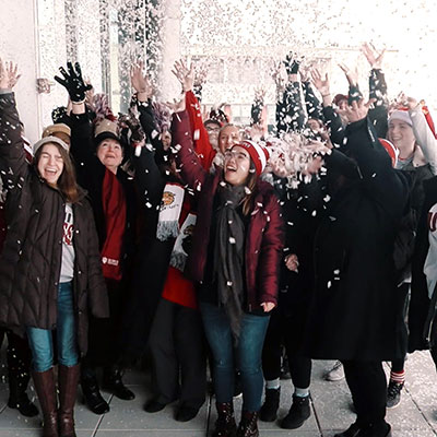 Chancellor Paydar stands in the middle of a group of celebratory students on the outdoor terrace of the Campus Center. All are dressed in winter gear and confetti hangs in the air.  