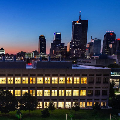 IUPUI building with lights on and Indianapolis skyline in the background.  Evening shot with deep blue sky.