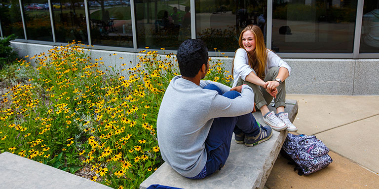Students chatting on a bench beside a bed of black-eyed susans